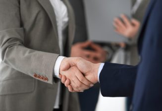 Business people shaking hands at meeting or negotiation, close-up. Group of unknown businessmen and women in modern office at background. Teamwork, partnership and handshake concept